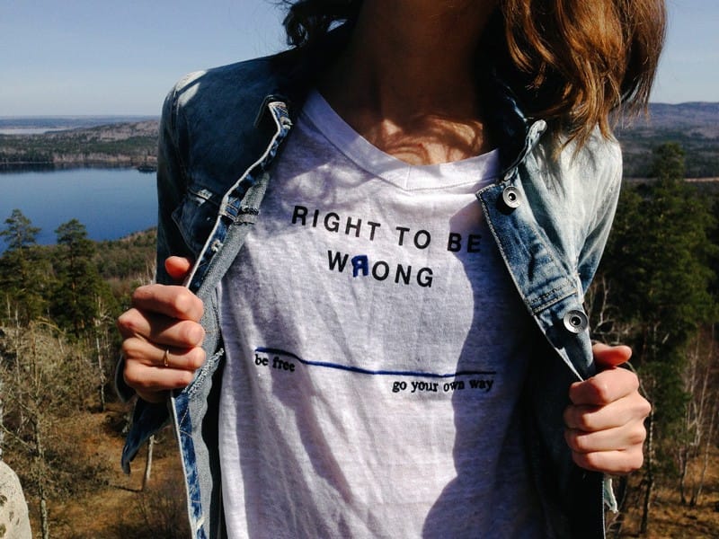 Sufragio femenino chica que enseña una camiseta blanca y un mensaje en inglés sobre el derecho a equivocarse. Lleva una chaqueta tejana y de fondo se ve el mar